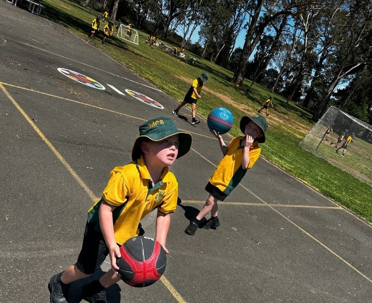 2 boys playing basketball and playground in background